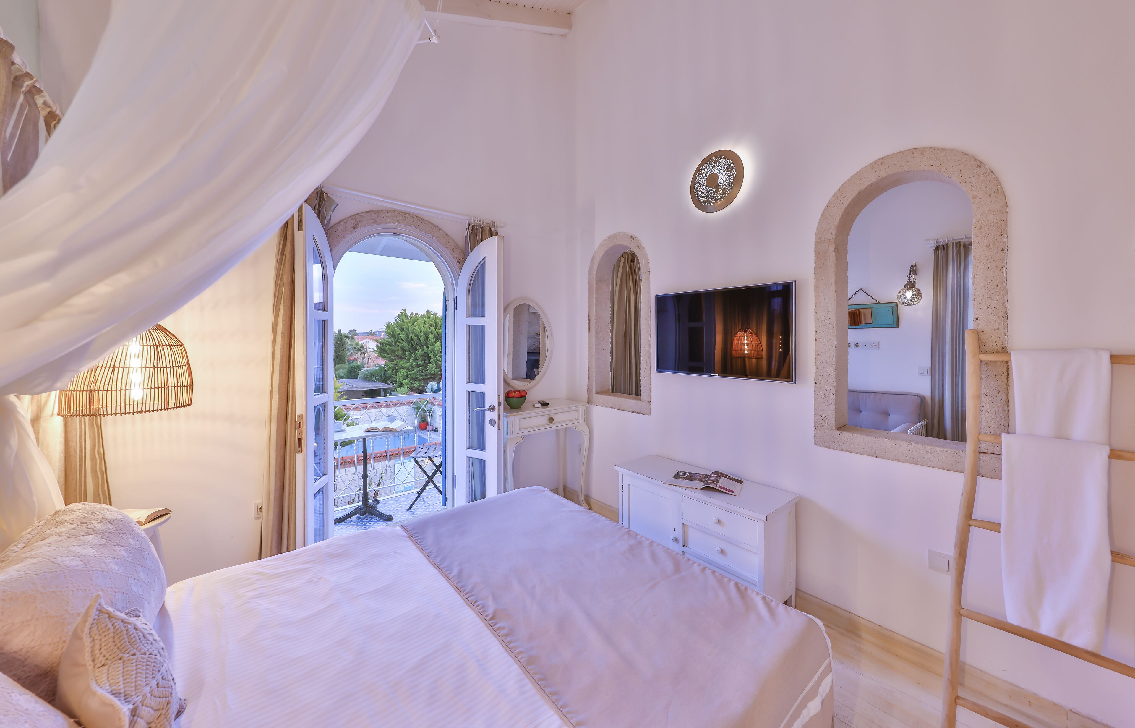 Un dormitorio con una cama grande, televisor, ventana con cortinas y vistas al balcón.