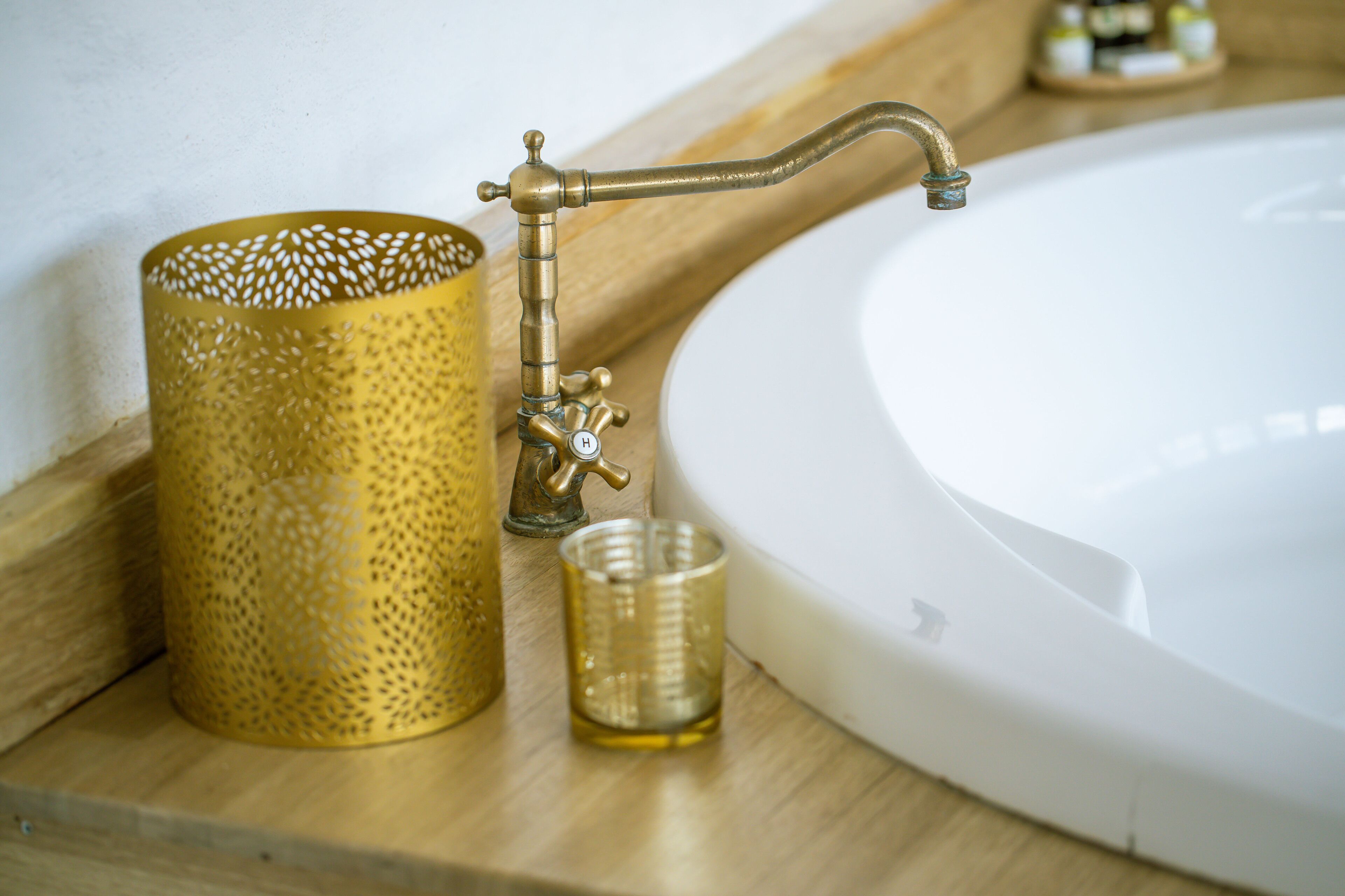 Un lavabo de salle de bain avec un robinet en laiton, un récipient perforé doré et un verre transparent.