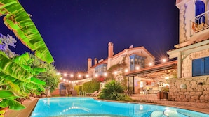 Una piscina con borde de baldosas, rodeada de abundante vegetación y un muro de piedra.