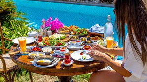Una mesa de comedor con diversos platos y bebidas, al lado de una piscina.