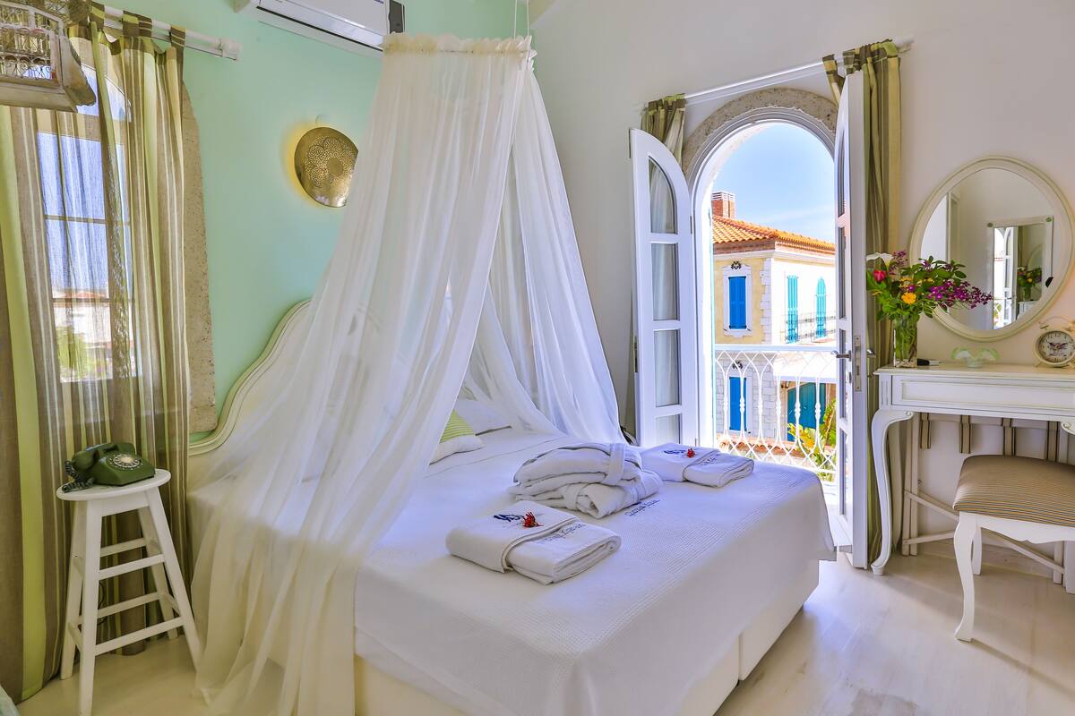 A bedroom with a bed, a vanity, a chair, a bedside table, and a window with curtains.