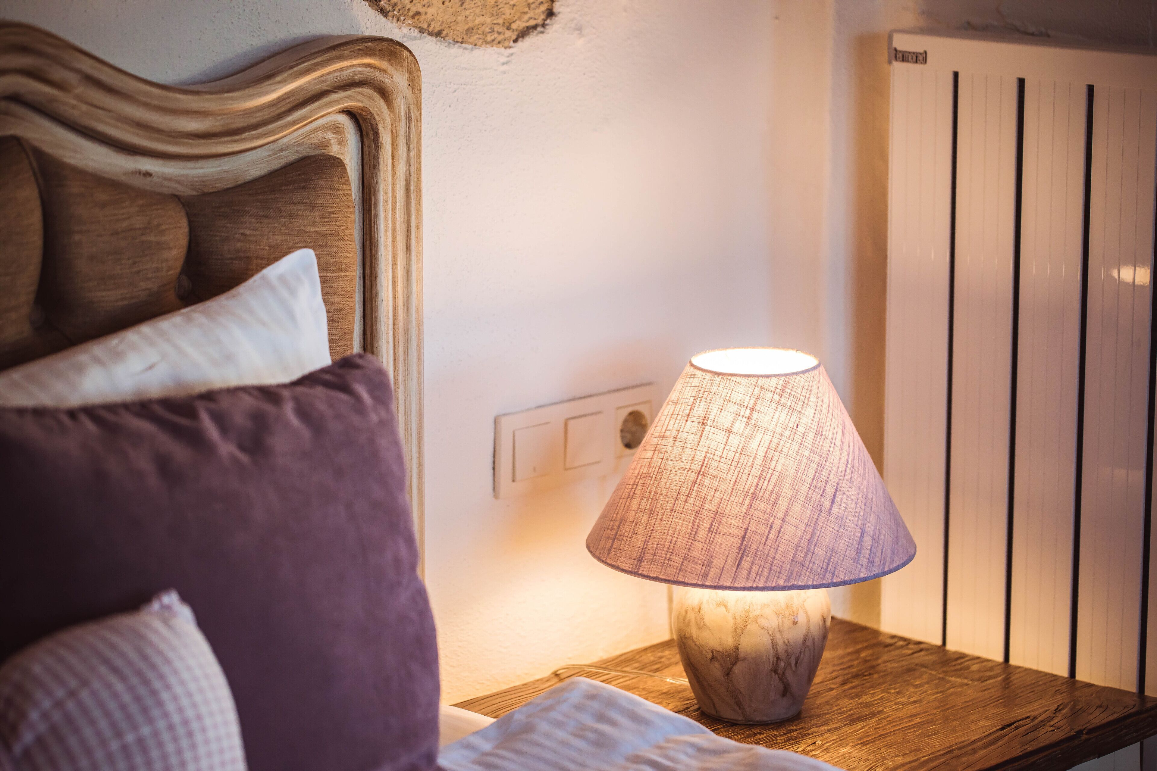 A bedroom with a wooden headboard, a bedside table with a lamp, and a radiator.