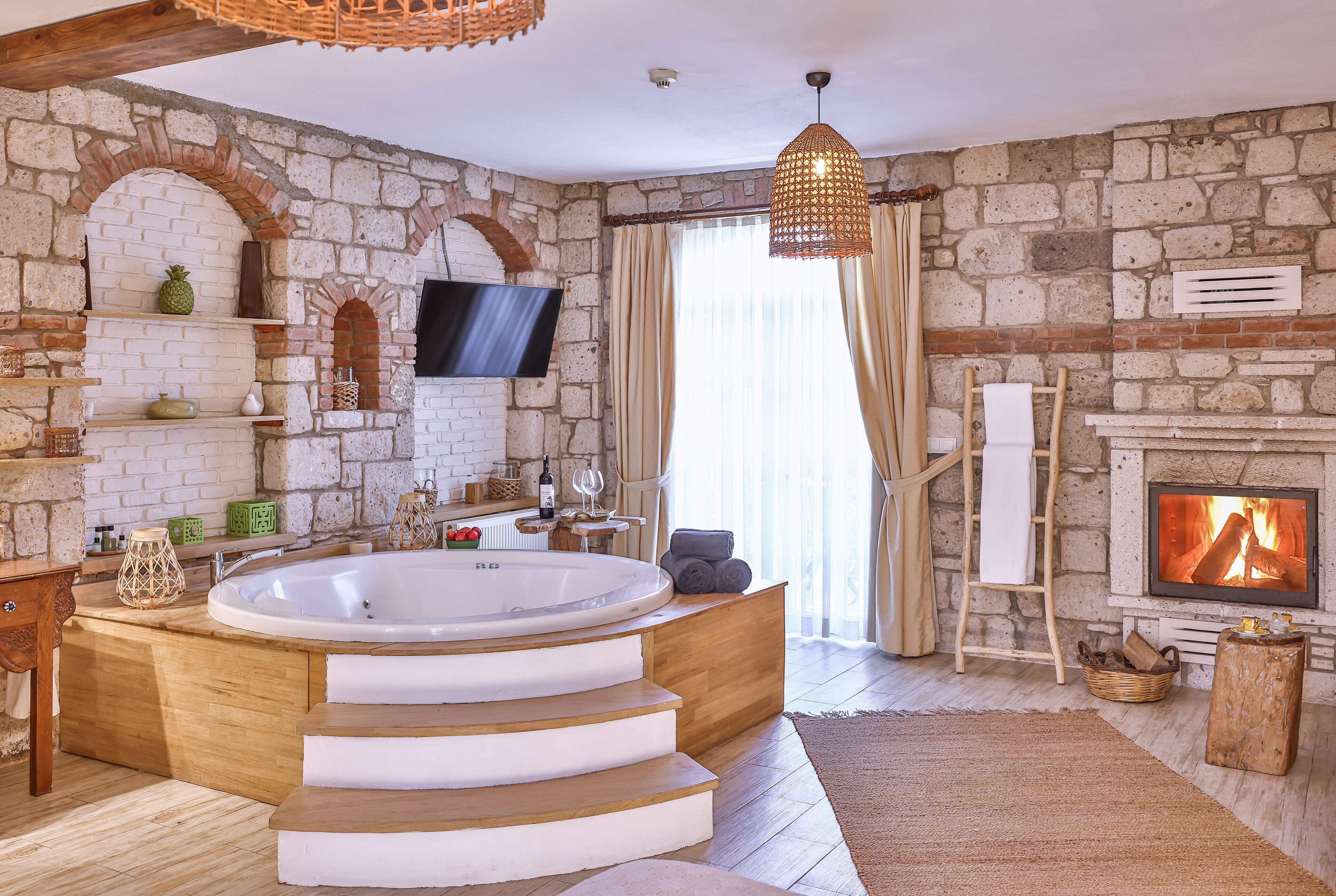 A room with a stone wall, a fireplace, a large bathtub, and a television.