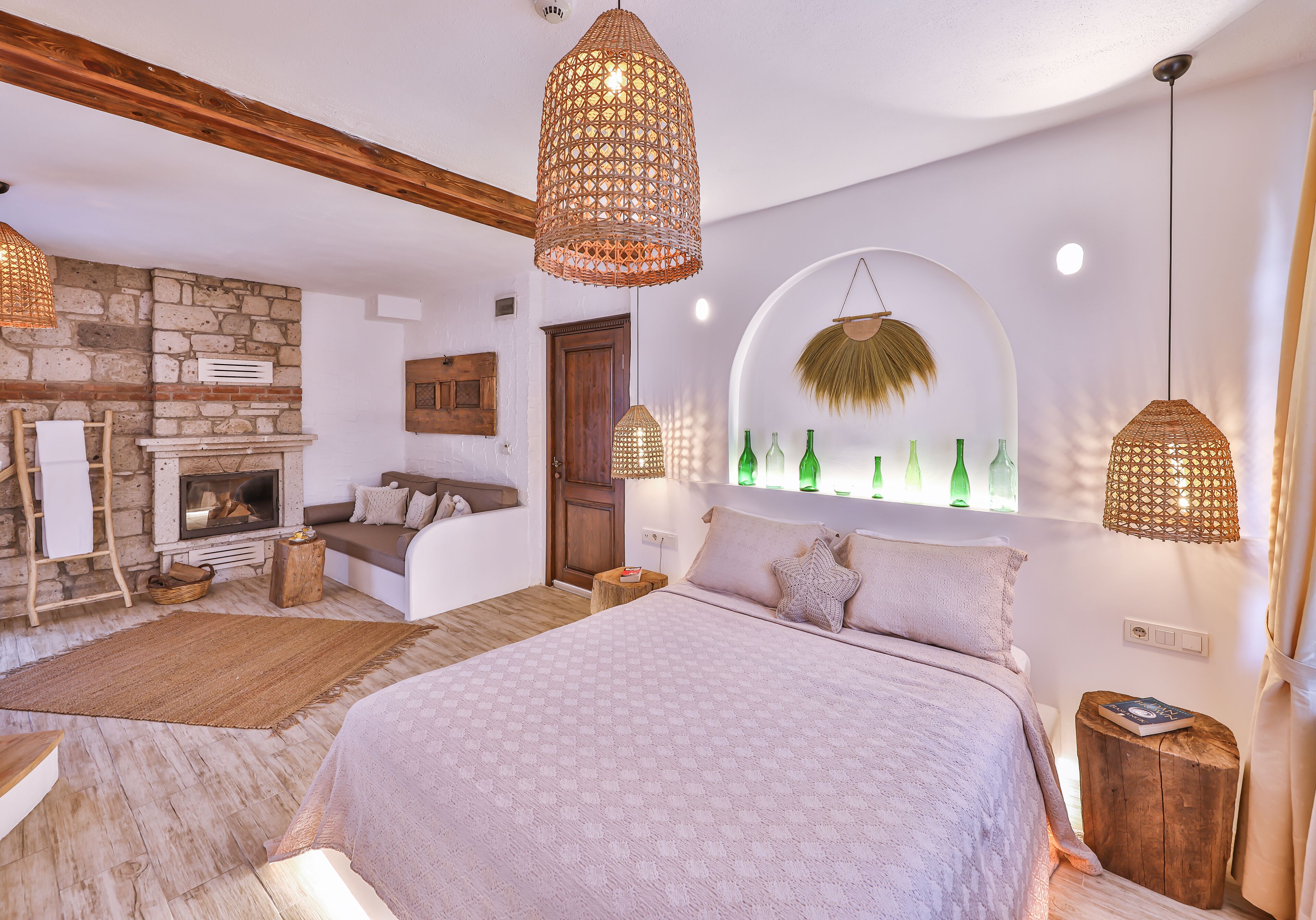A bedroom with a large bed, a stone fireplace, and hanging wicker lamps.