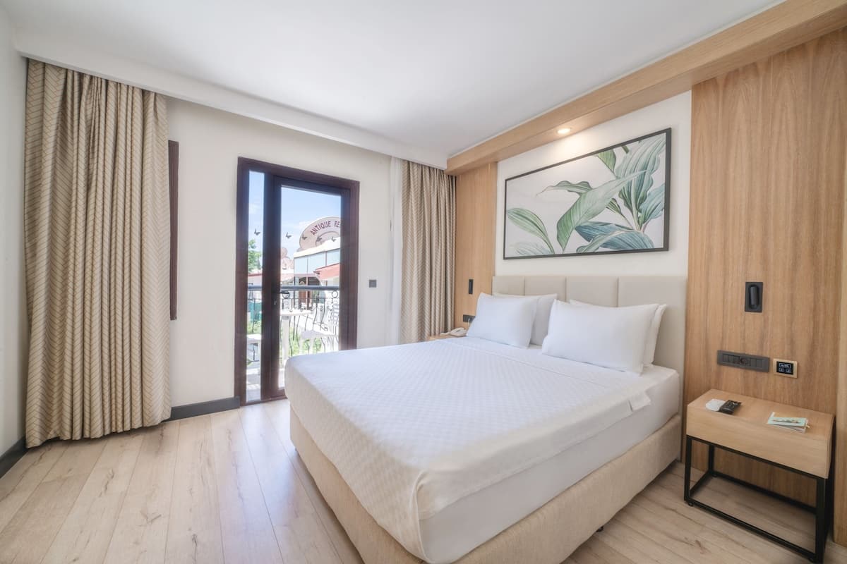 A hotel room with a large bed, a wooden headboard, a small bedside table, and a view of the outside balcony.