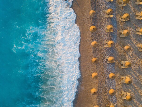 An aerial view of a beach with rows of umbrellas and lounge chairs, indicating a beach resort setting. - Sundia By Liberty Ölüdeniz (Fethiye)