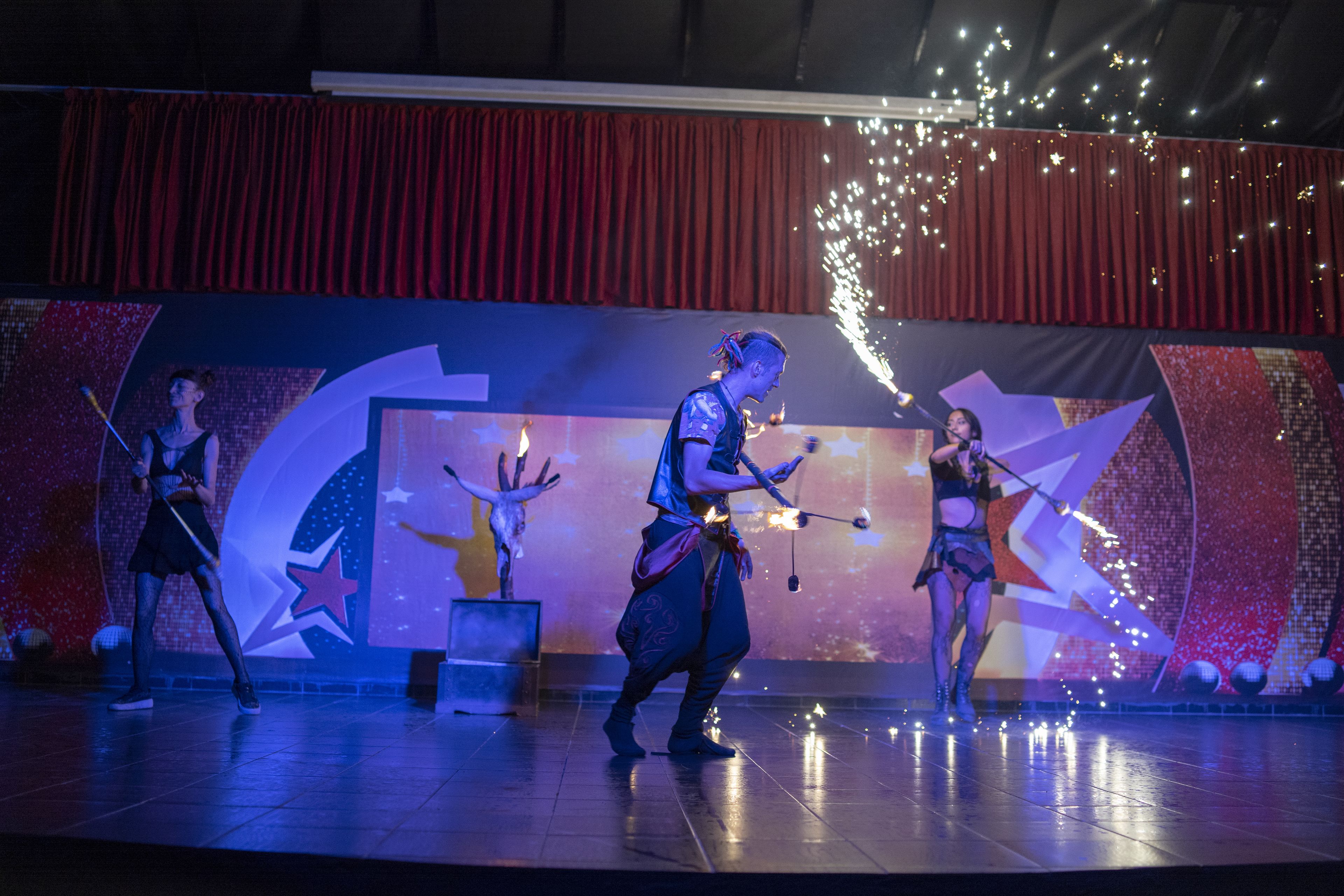 Um palco com artistas, um fundo de cortina vermelha e um design com tema de estrelas.