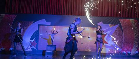 Um palco com artistas, um fundo de cortina vermelha e um design com tema de estrelas.