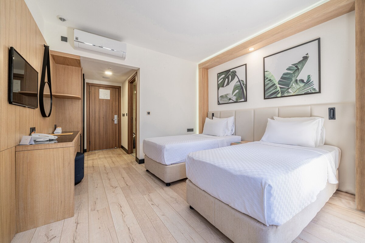A hotel room with two beds, a desk, and a mirror.