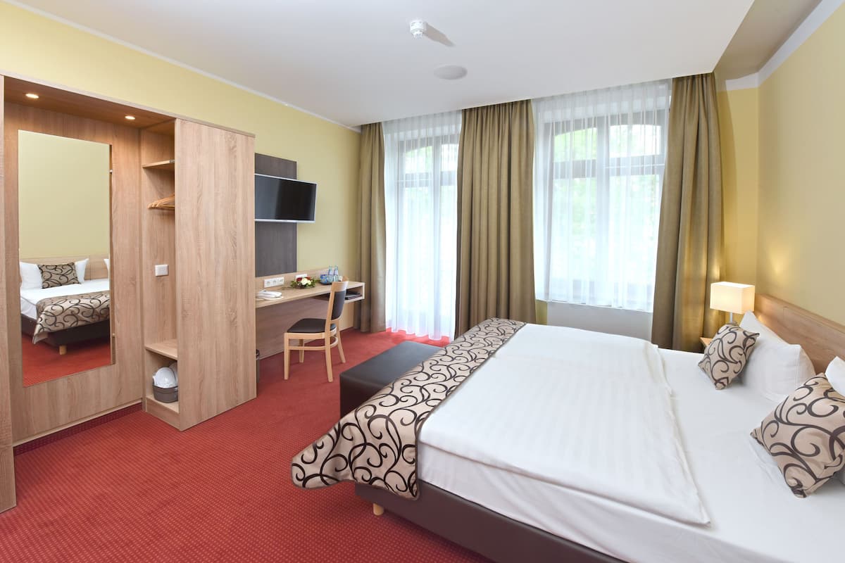 Ein Hotelzimmer mit Bett, Schreibtisch, Stuhl, Fernseher und Kleiderschrank.