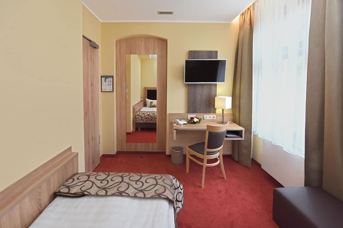 Ein Hotelzimmer mit Bett, Schreibtisch, Stuhl, Fernseher und einem fensterbepflanzten Fenster.