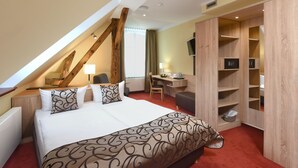 Ein Hotelzimmer mit einem großen Bett, einem Schreibtisch, einem Sessel, einem Fernseher und einem Kleiderschrank.