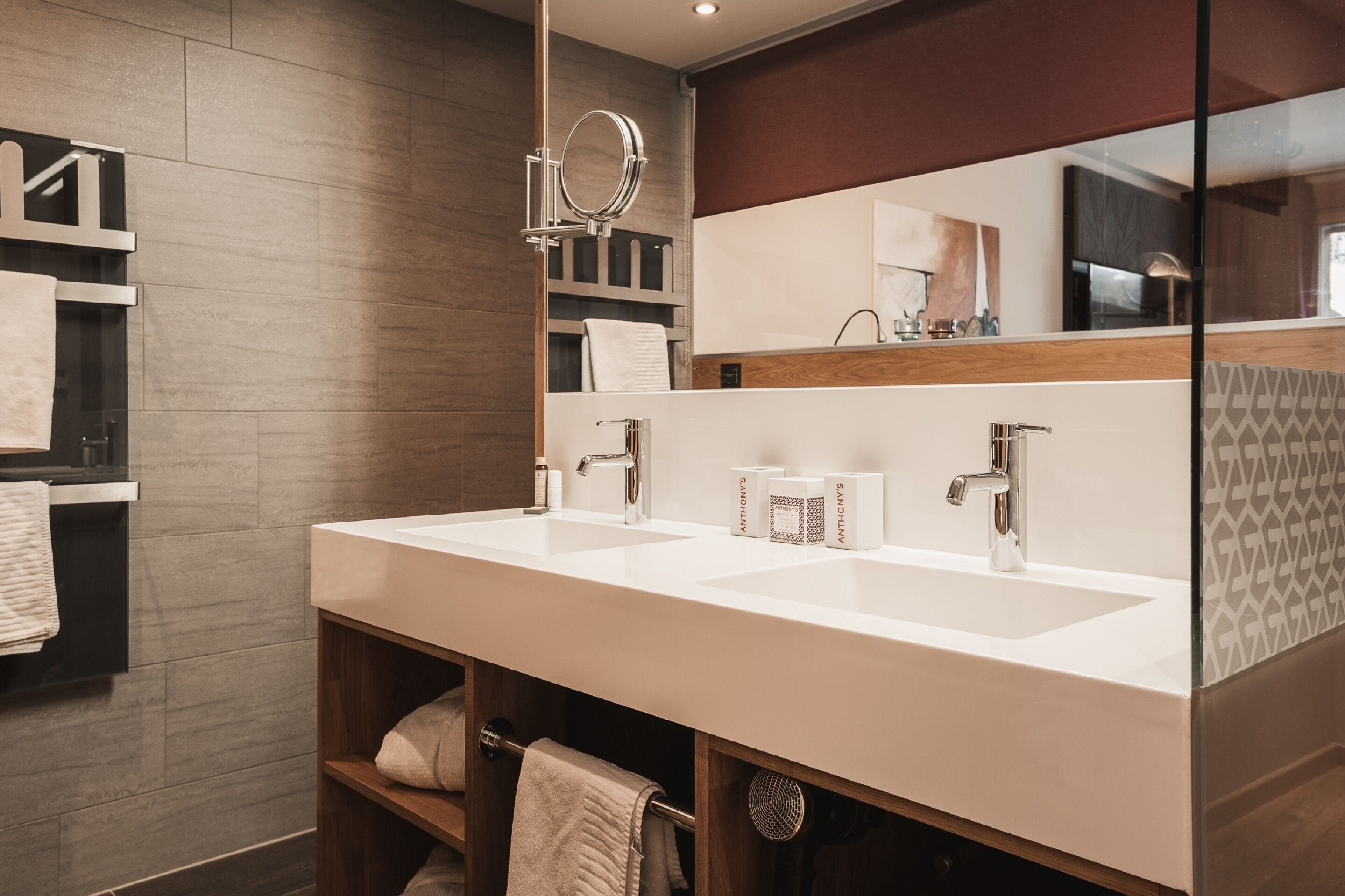 A modern bathroom with two sinks, a large mirror, and a towel rack.