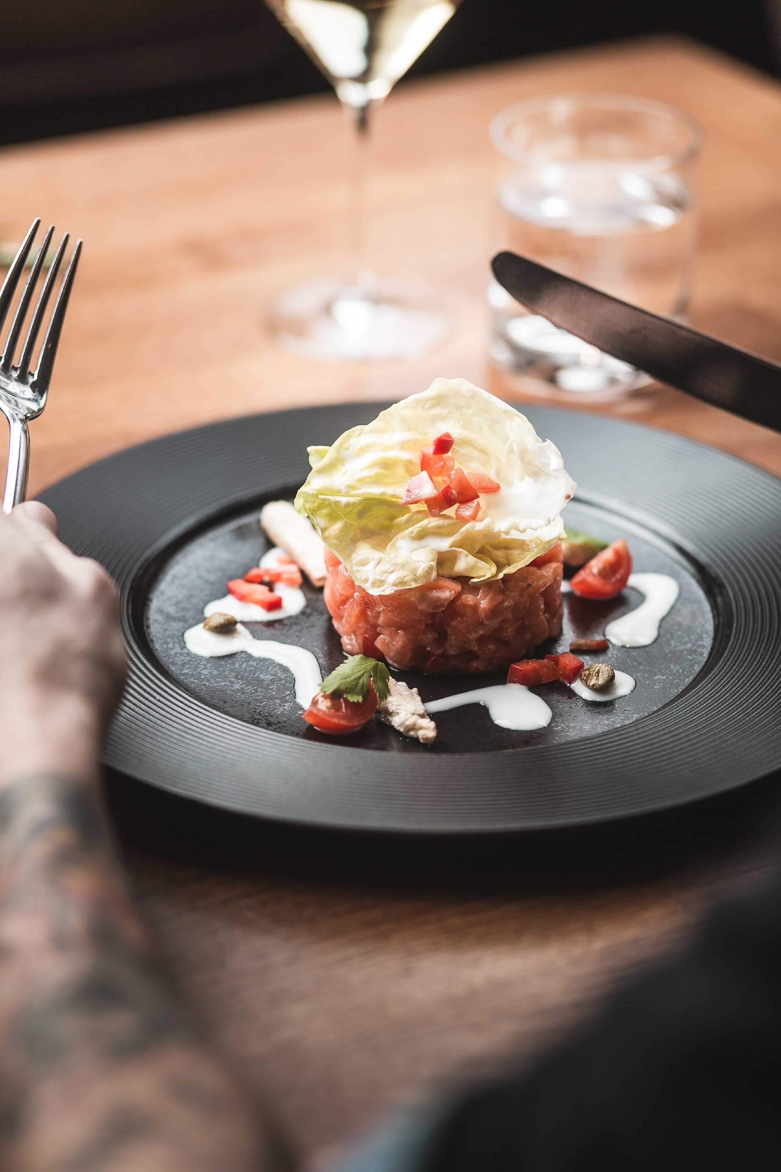 A plate of food with a fork and knife on the side, a glass of water, and a wine glass in the background.