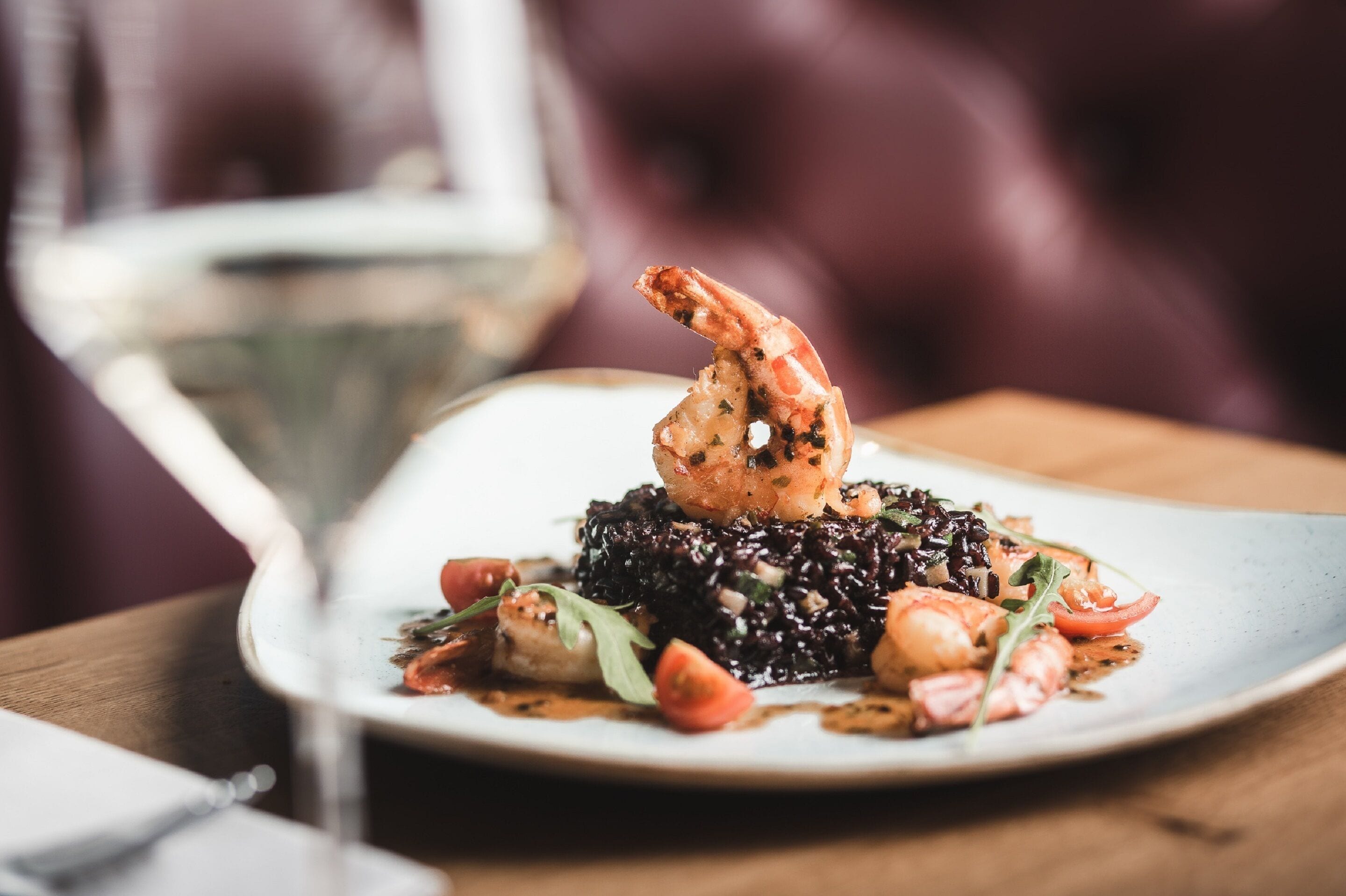 A plate of food with shrimp and vegetables, a glass of white wine, and a wooden table.