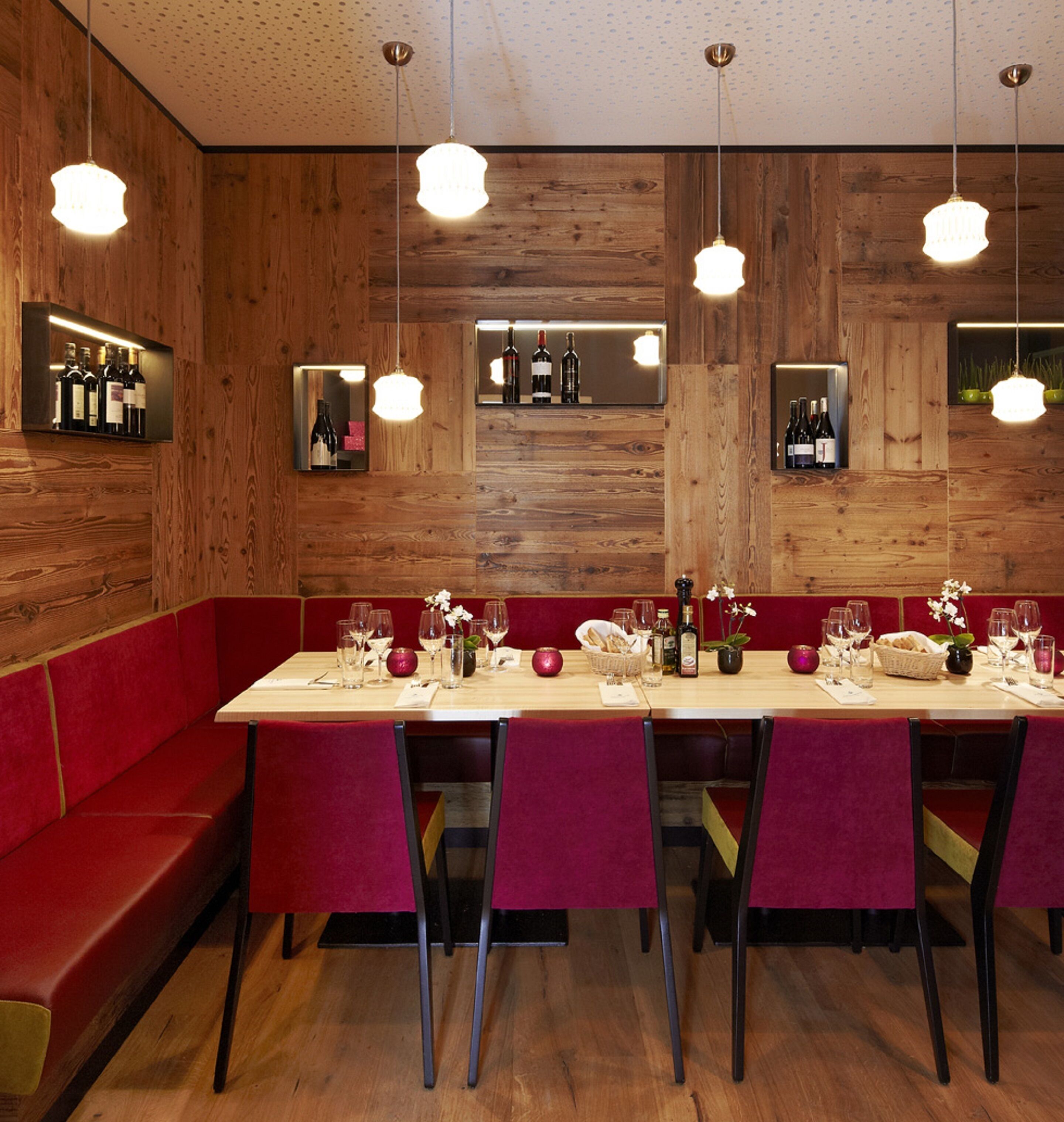 A restaurant with wooden walls, red seating, and a long dining table set with wine glasses and bottles.