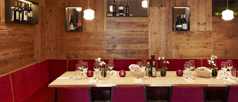 A restaurant with wooden walls, red seating, and a long dining table set with wine glasses and bottles.