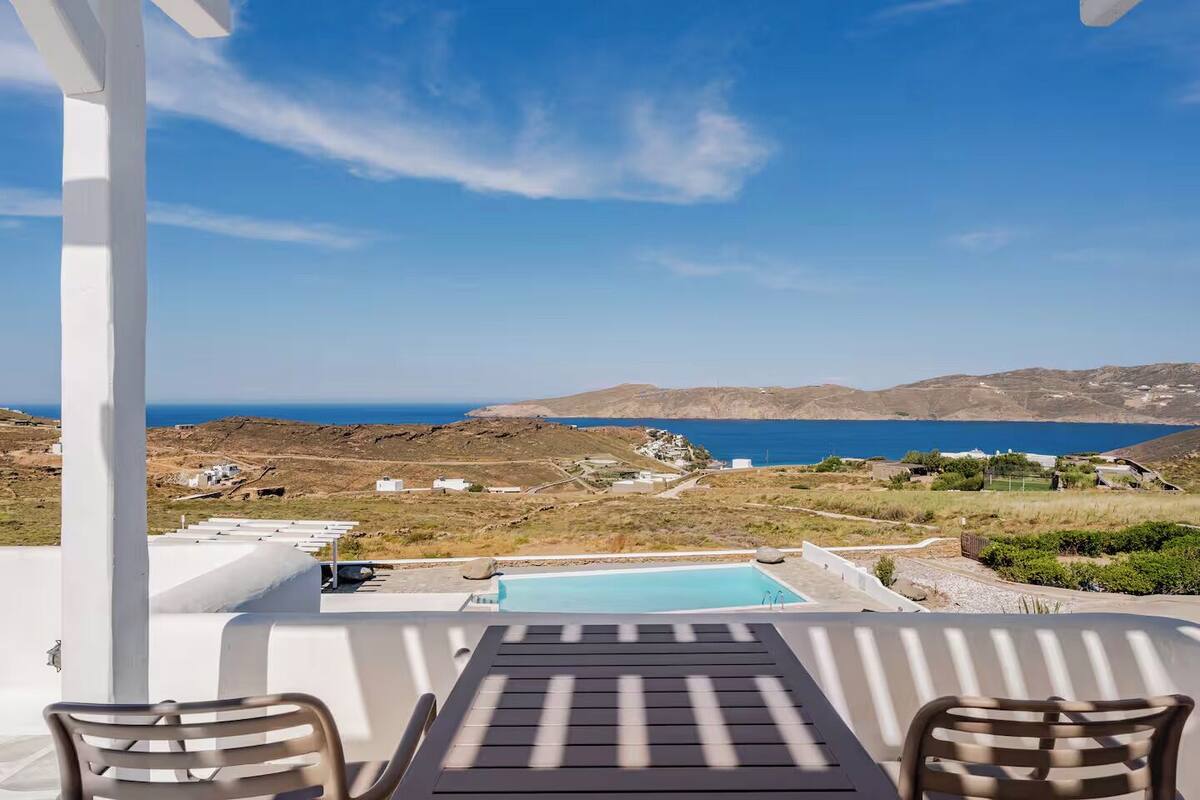 Une terrasse avec une piscine, deux chaises et une table donnant sur un paysage côtier.