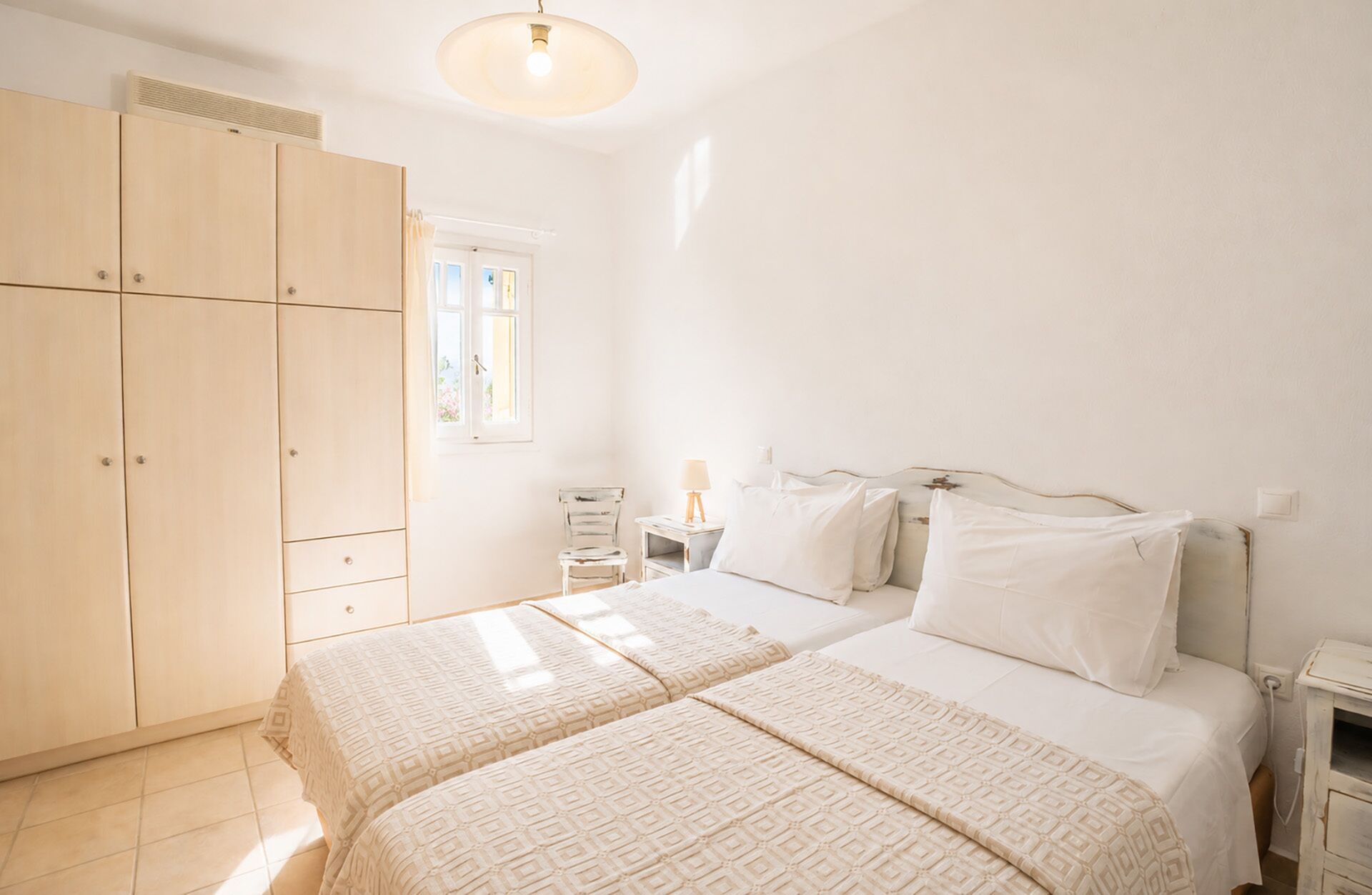 A bedroom with two beds, a wardrobe, a bedside table with a lamp, and a window with curtains.
