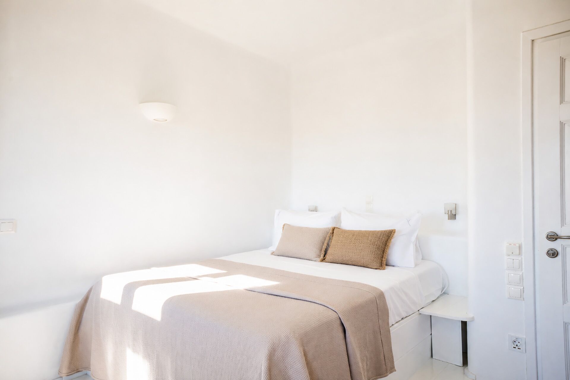 A minimalist bedroom with a bed, bedside tables, and a door.