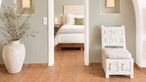 A bedroom with a bed, a nightstand, a vase with plants, and a chair. - Yakinthos Residence (Mykonos)