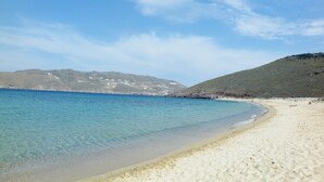 A beach with clear blue water, sandy shore, and a hilly background. - Yakinthos Residence (Mykonos)