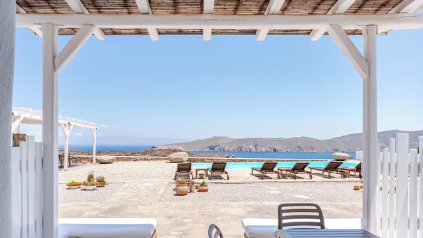 A covered outdoor area with a pool, lounge chairs, and potted plants. - Yakinthos Residence (Mykonos)