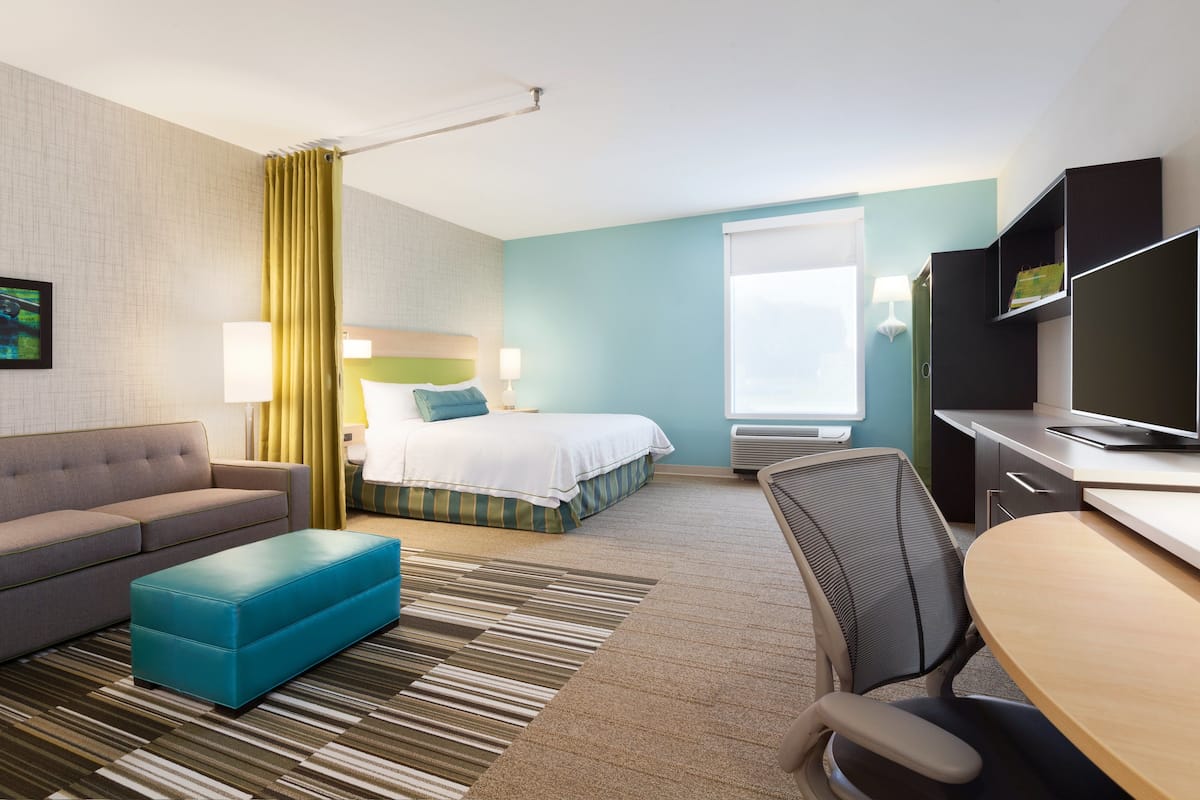 A hotel room with a bed, a sofa, a desk, and a television.