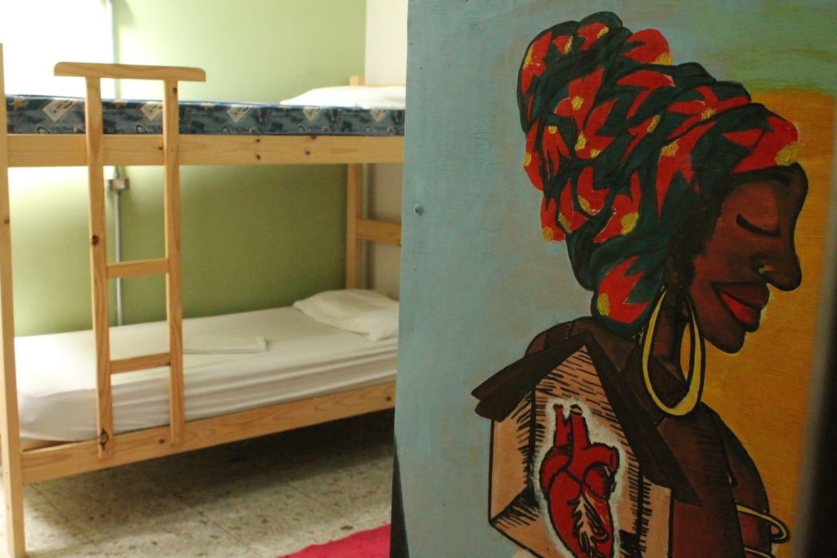 Ein Etagenbett mit Holzrahmen und weißer Bettwäsche, ein Bild von einer Frau mit einem Herz und eine grüne Wand.