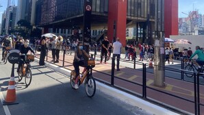 A busy urban street with cyclists and pedestrians, a prominent red building, and a clear blue sky. - Nomade In Arte e Hostel São Paulo (São Paulo)