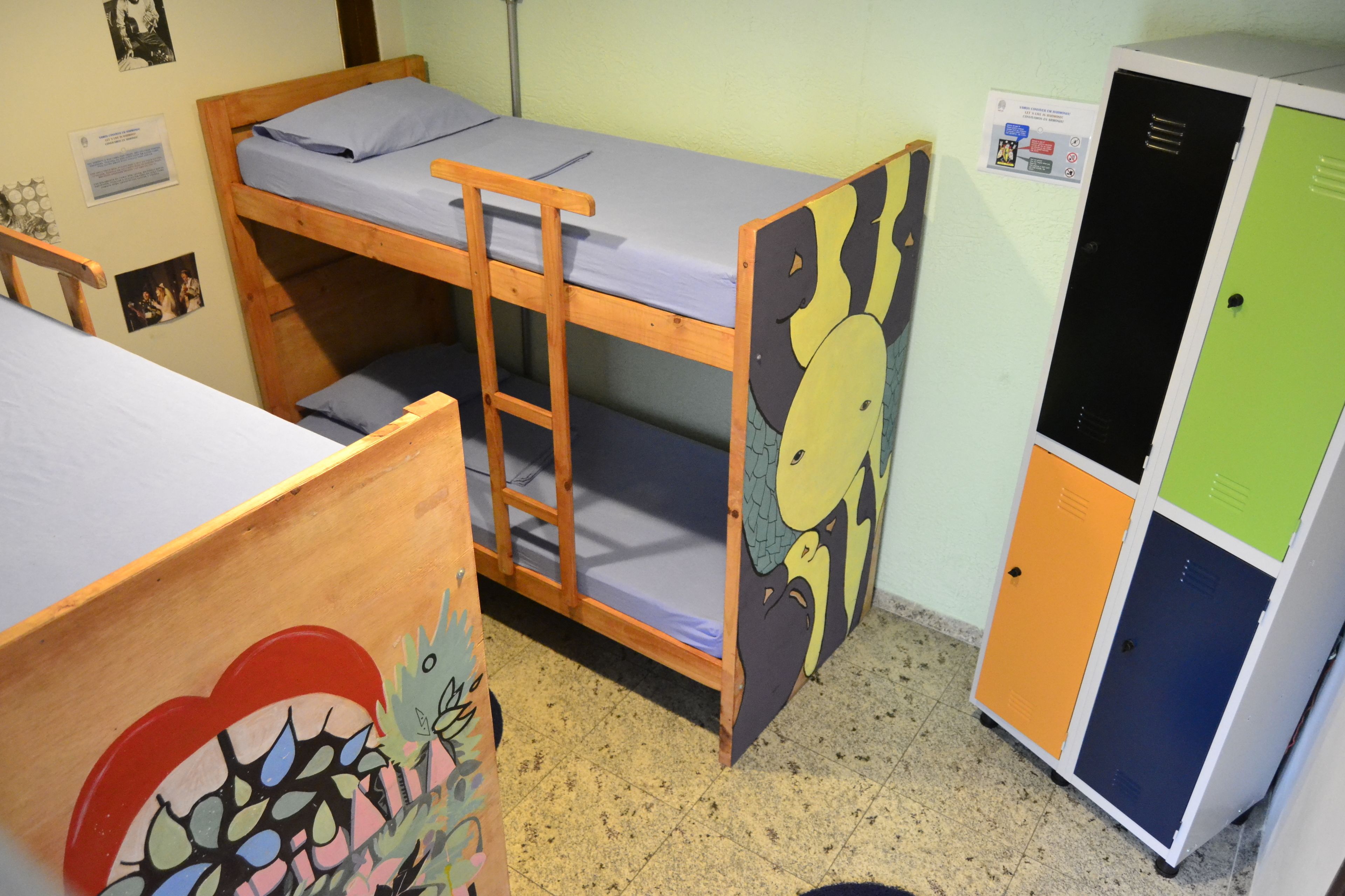 A dormitory room with bunk beds, a wooden desk, and a colorful locker.