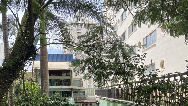 An outdoor seating area with tables and chairs, surrounded by greenery and a building in the background. - Nomade In Arte e Hostel São Paulo (São Paulo)