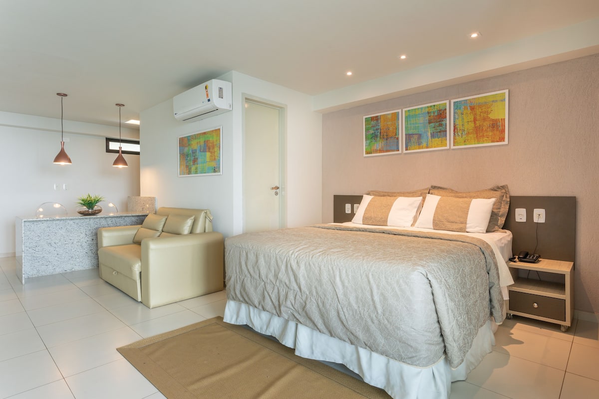 A modern bedroom with a large bed, a bedside table, a chair, and a small desk area.