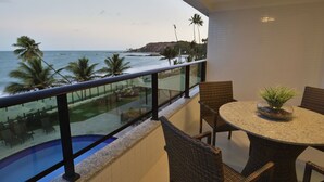 Un balcone con vista sull'oceano, una piscina e un'area pranzo con sedie in vimini e un tavolo.