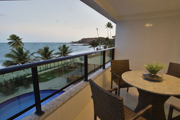A balcony with a view of the ocean, a pool, and a dining area with wicker chairs and a table. - Nord Life Tabatinga (João Pessoa)