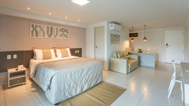A modern hotel room with a large bed, a small desk, a kitchenette, and a seating area. - Nord Life Tabatinga (João Pessoa)
