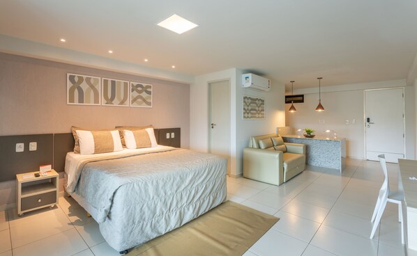 A modern hotel room with a large bed, a small desk, a kitchenette, and a seating area. - Nord Life Tabatinga (João Pessoa)