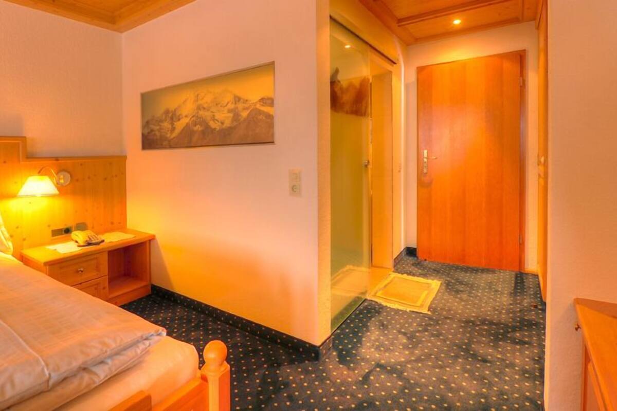 A bedroom with a bed, bedside table, lamp, and a painting on the wall.