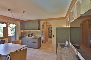 A modern kitchen with wooden cabinets, a dining table, and chairs. There is a chandelier above the table and a kitchen island with a sink and countertop. - Die Seefelderin - Boutiquehotel St. Georg (Seefeld in Tirol)