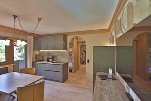 Una cocina moderna con armarios de madera, una mesa de comedor y sillas. Encima de la mesa hay una araña y una isla de cocina con un lavamanos y una encimera.