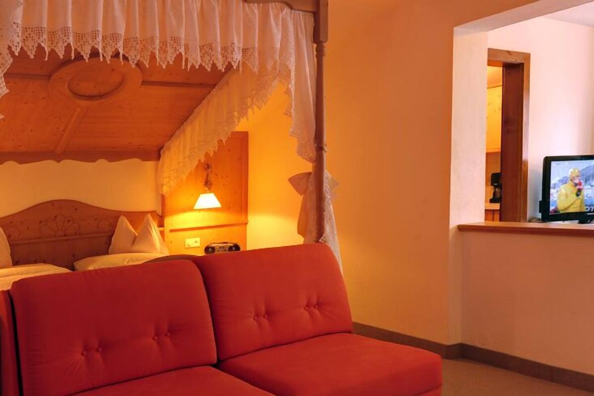 A cozy room with a four-poster bed, a red sofa, and a television on a wooden table.
