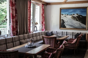 Una zona relax accogliente con un divano e poltrone, un tavolo con una candela e un quadro di un paesaggio montano.