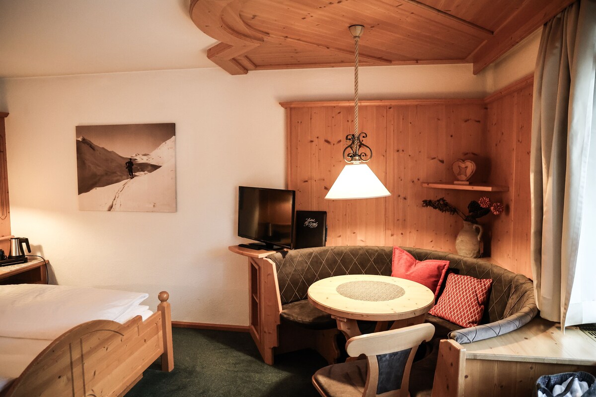 A cozy room with a bed, a sofa, a television, and a wooden ceiling.