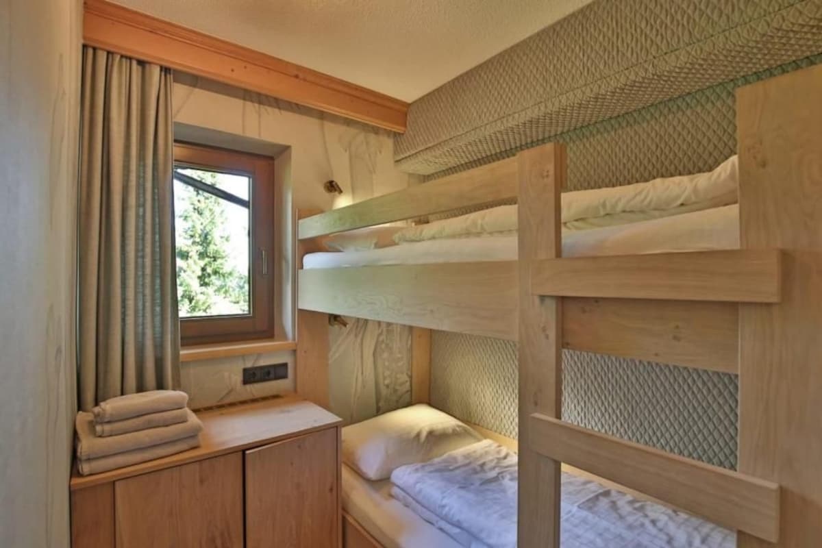 A bunk bed room with a window, wooden headboard, and a small bedside table with a towel.