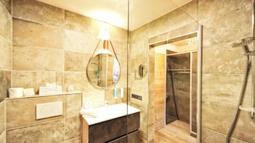 Un baño moderno con ducha envuelta en vidrio, un espejo redondo y un tocador de madera.