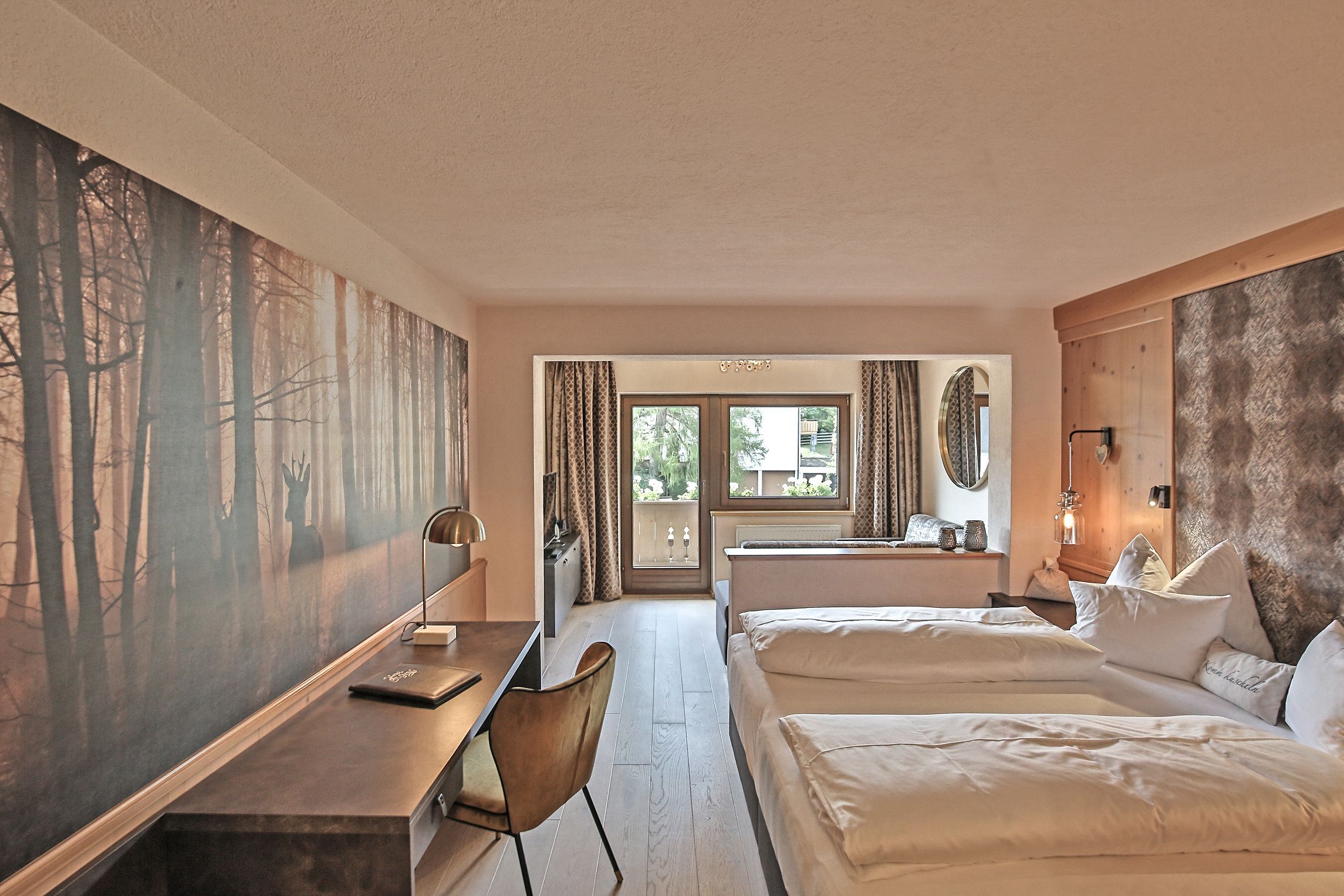 Ein Hotelzimmer mit Schreibtisch, zwei Betten, einem großen Gemälde und Blick ins Freie.