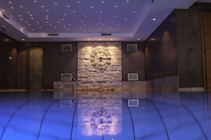 A spacious room with a reflective floor, a stone wall with a clock, and a ceiling with a star-like pattern. - Die Seefelderin - Boutiquehotel St. Georg (Seefeld in Tirol)