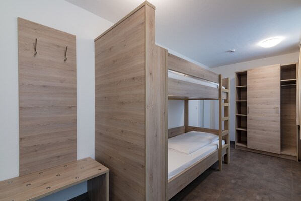 Una cama litera con acabado de madera, un escritorio con superficie de madera y un armario de puertas abiertas.
