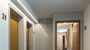 Un pasillo con puertas numeradas 21 y 23, pisos alfombrados y una puerta de madera a la izquierda.