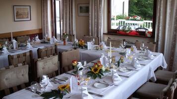 A dining area with multiple tables set for a meal, featuring white tablecloths, neatly arranged cutlery, and floral centerpieces.